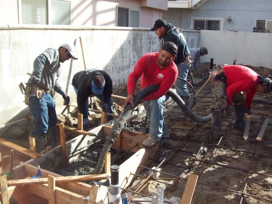 Crew of six men pouring concrete over footings for a new foundation