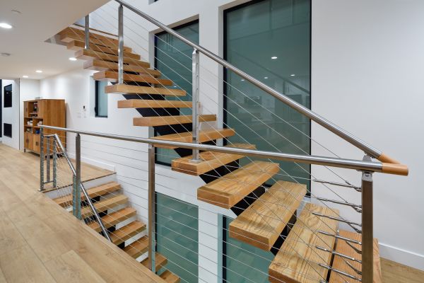 Custom floating staircase and stainless railing in front of large glass windows on second floor