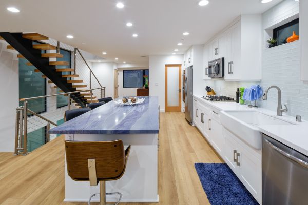 Custom white kitchen with blue stone counter at island and wood floors next to floating stairs