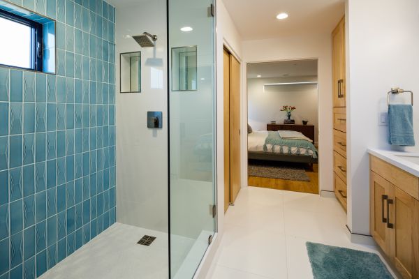 Beautiful ensuite master bath with turquoise tiles & glass & built-in wood cabinets showing master bedroom beyond