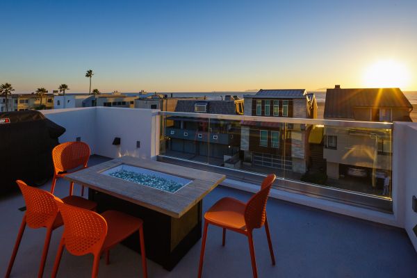 Red chairs surround a gas firepit table on a rooftop deck overlooking the Pacific Ocean