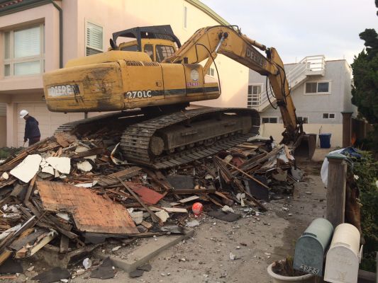 Large yellow bulldozer atop wreckage of a demolished beach shack